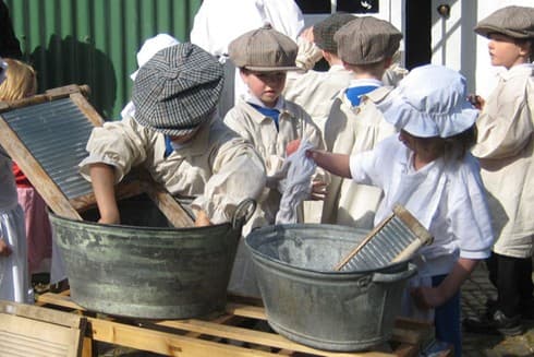 Children washing clothes in a bucket, dressed in victorian gear.